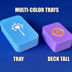 Puede incluir: Dos bandejas rectangulares, una azul claro y otra morada, se muestran sobre una superficie azul. La bandeja azul claro tiene un diseño blanco y la bandeja morada tiene un diseño dorado. El texto en la imagen dice "MULTI-COLOR TRAYS", "TRAY" y "DECK TALL".