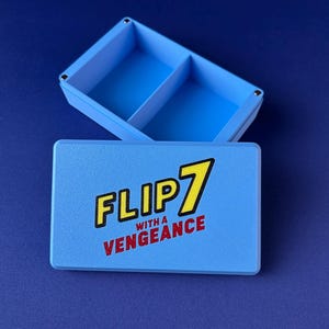 Puede incluir: Una caja azul claro con tapa, con el texto "FLIP 7 with a Vengeance" en amarillo y rojo. La caja est&aacute; dividida en dos compartimentos. El fondo es azul oscuro liso.