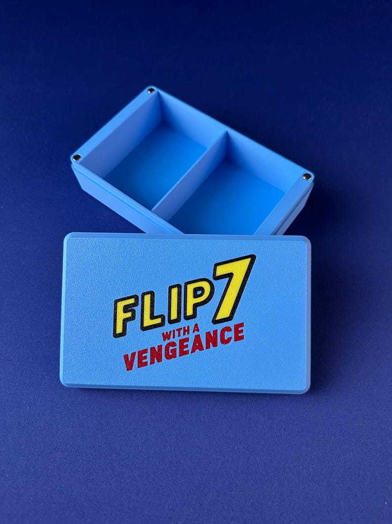 Puede incluir: Una caja azul claro con tapa, con el texto "FLIP 7 with a Vengeance" en amarillo y rojo. La caja est&aacute; dividida en dos compartimentos. El fondo es azul oscuro liso.
