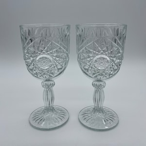 May include: Two clear wine glasses with a diamond and starburst pattern. Each glass has a ribbed stem and a circular base with radiating lines. The glasses are made of clear glass. The height of the glasses is approximately 15 cm.