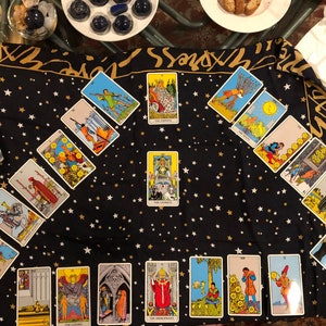 May include: A tarot card reading spread laid out on a black fabric with gold stars. The cards are arranged in a diamond shape with the Emperor card in the center. The cards are from the Rider-Waite tarot deck.