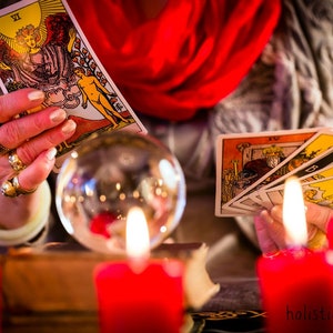 May include: A tarot card reading with a crystal ball, candles, and several tarot cards spread out on a table. The card being held is the 'The Star' card, which is the 17th card in the Major Arcana.