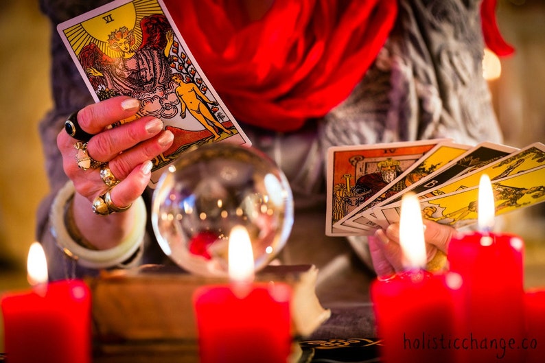 May include: A tarot card reading with a crystal ball, candles, and several tarot cards spread out on a table. The card being held is the 'The Star' card, which is the 17th card in the Major Arcana.
