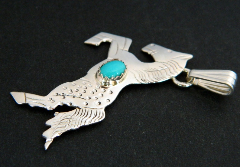 May include: A silver pendant featuring a stylized horse design with a turquoise stone set in the center. The pendant has a loop for attaching to a chain.