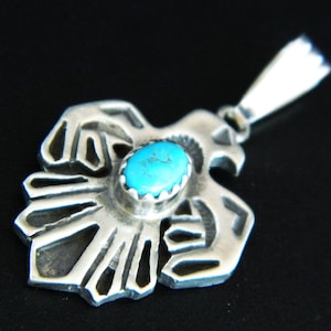 May include: Sterling silver pendant featuring a detailed eagle design with a turquoise stone in the center. The pendant has a bail for attaching to a chain.
