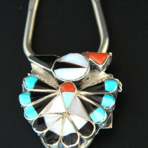 May include: A silver key chain with a turquoise, black, white, and red stone inlay design. The design is a stylized bird with a fan-shaped tail.