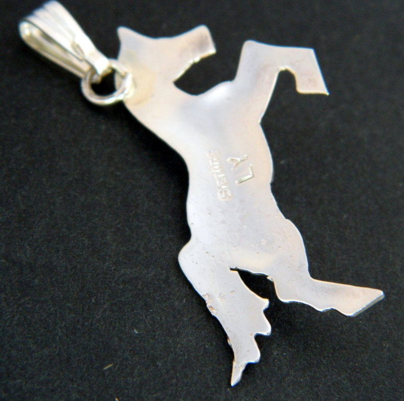 May include: Silver pendant in the shape of a rearing horse. The back of the pendant is stamped with "Sterling" and "LY".
