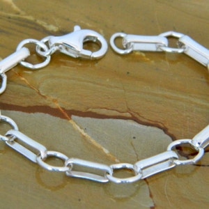 May include: A silver chain bracelet with a lobster clasp closure. The chain is made of rectangular links.
