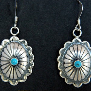 May include: A pair of silver earrings with turquoise stones. The earrings are oval shaped and have a sunburst design.
