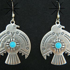 Puede incluir: Un par de pendientes plateados con forma de pájaro, con una piedra turquesa en el centro. Los pendientes tienen intrincados diseños estampados y están suspendidos de un gancho simple.