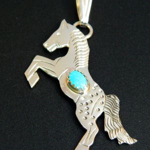 May include: Sterling silver pendant featuring a rearing horse design with a turquoise stone inlay. The horse is detailed with textured lines and dots.