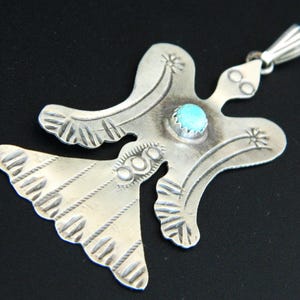 May include: A silver pendant in the shape of a bird, with a turquoise stone at its centre. The pendant has detailed etched patterns and a loop for hanging. The design includes floral and geometric patterns.