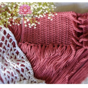 May include: A close-up of a pink crocheted scarf with fringe. The scarf is made with a textured stitch and has a delicate, feminine look.