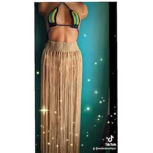 May include: A beige crochet skirt with long fringe. The skirt is worn over a black and blue striped bikini top.
