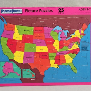 May include: A 25-piece picture puzzle featuring a map of the United States with each state labeled. The puzzle is on a pink background with the words "Puzzle Patch Picture Puzzles" and "Ages 3-7" printed on it.