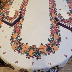 May include: A white oval tablecloth with a burgundy and green floral border featuring a repeating pattern of leaves, berries, and flowers. The tablecloth has a burgundy and white border with a floral pattern.