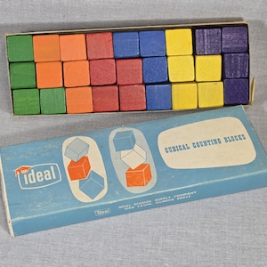 May include: A vintage set of Ideal Cubical Counting Blocks in a box. The blocks are in various colors, including green, orange, red, blue, yellow, and purple. The box is light blue with the Ideal logo and the text "Cubical Counting Blocks".