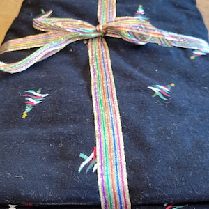 May include: A black fabric gift bag with a colorful ribbon tied around it. The bag is decorated with small embroidered Christmas trees.