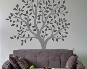 May include: A gray tree wall decal with a simple design, featuring a thick trunk and many branches with leaves. The decal is applied to a white wall above a brown couch.