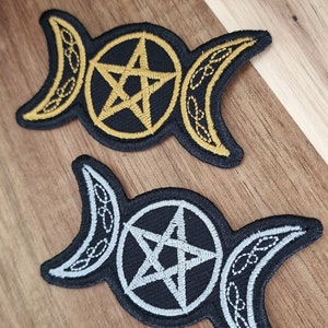 May include: Two embroidered patches featuring the triple moon symbol and a pentagram. One patch is gold on black fabric, and the other is silver on black fabric.