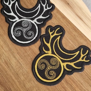 May include: Two embroidered patches with a black background and a gold or silver Celtic knot design. The knot is surrounded by a circle with antlers on either side.