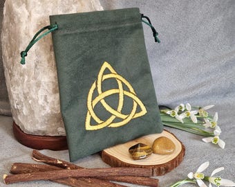 May include: A green velvet pouch with a gold embroidered Celtic knot design. The pouch is sitting on a wooden surface with two stones and sticks.