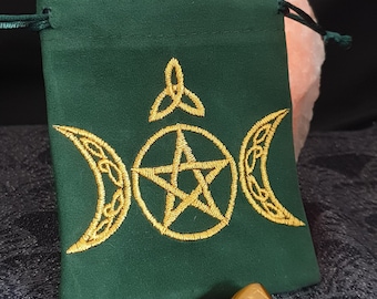 May include: Green velvet pouch with a gold embroidered triple moon, pentagram, and Celtic knot design. Two tiger's eye stones are in front of the pouch.