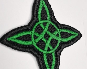May include: A four-pointed star-shaped embroidered patch featuring a black background with a vibrant green stitched design. The pattern consists of a central circle with intersecting lines that extend into each of the four pointed tips.