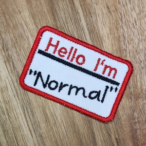 May include: Red and white embroidered patch with the text "Hello I'm "Normal""