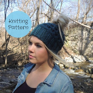 May include: A teal knitted hat with a messy bun opening. The hat has a ribbed brim and a textured stitch pattern. A light blue circle with the words "Knitting Pattern" is in the upper left corner. The hat is worn by a person with blonde hair.