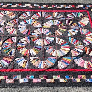 May include: A black and red quilt with a unique design featuring a pattern of colorful fabric circles. The quilt is made with a variety of fabrics and has a red border.