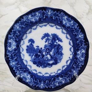 May include: A blue and white porcelain plate with a decorative border and a central image of a couple in a garden setting.