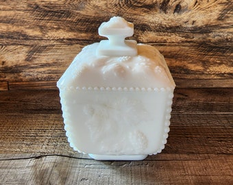 Puede incluir: Plato de dulces de vidrio de leche blanco con forma cuadrada y un diseño floral en relieve. La tapa tiene un pomo en la parte superior.