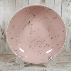 May include: A pink ceramic bowl with a black marbled design. The bowl is on a white wooden surface.