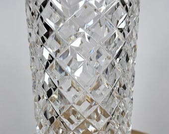 Puede incluir: Un vaso de cristal tallado transparente con un patrón de diamantes. El vaso es cilíndrico con un borde ligeramente ensanchado y se asienta sobre una base redonda. El intrincado diseño captura y refleja la luz, creando un efecto brillante.