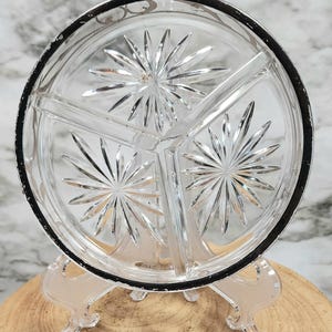 May include: A clear glass divided serving dish with a silver rim. The dish has three sections and a starburst pattern.
