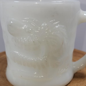 May include: White ceramic mug with a raised design of a palm tree. The mug has a handle and is made of opaque white ceramic.