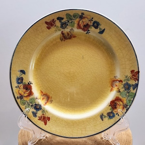 May include: A vintage yellow ceramic plate with a floral design. The plate features a cracked glaze and a dark blue rim. The floral pattern includes red, orange, and blue flowers with green leaves, adding a touch of elegance to the tableware.