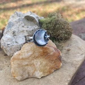 May include: A silver ring with a crescent moon and star design. The moon is made of iridescent mother of pearl.