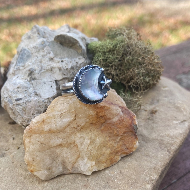 May include: A silver ring with a crescent moon and star design. The moon is made of iridescent mother of pearl.