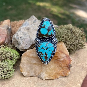 May include: A sterling silver ring with two turquoise stones set in a triangular shape. The turquoise is a mottled blue and brown color.