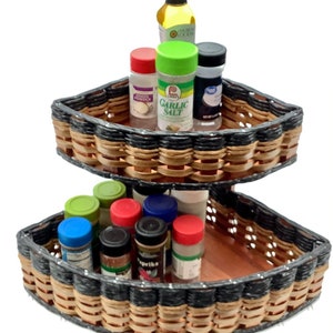 May include: Two-tiered wicker spice rack with a black and brown woven design. The top tier has three spice jars labeled "Onion Powder", "Garlic Salt", and "Sea Salt". The bottom tier has eight spice jars with various labels, including "Paprika".