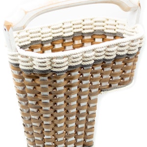 May include: A white wicker basket with a white wooden handle. The basket has a woven pattern with brown and white stripes. The basket is shaped like a letter 'T' and is perfect for storage.