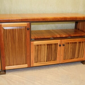 May include: A wooden entertainment center with a brown top, open shelves, and three doors. The doors are made of wood with a striped pattern and have metal handles.