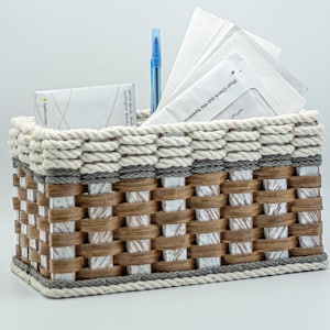 May include: A white wicker basket with a gray and white rope trim. The basket is filled with envelopes and a blue pen. The text on the envelopes reads "Please check out the special offers".