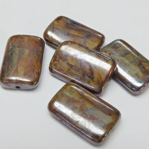 Peut inclure: Un ensemble de cinq perles rectangulaires à la finition lisse et polie. Chaque perle présente un motif marbré avec des tons mélangés de bronze métallique, de cuivre, de brun et de subtiles touches de vert et de bleu irisé sur la surface.