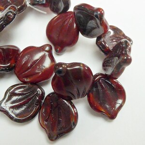 May include: A strand of dark red glass beads in the shape of flower petals. The beads have a glossy finish and are strung together on a clear thread.