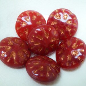 May include: Six red glass beads with a gold metallic design. The beads are round and have a glossy finish.