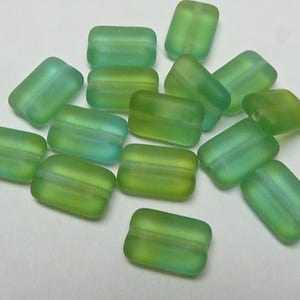 May include: A group of 14 green and blue glass beads with a frosted finish. The beads are rectangular in shape and have a slightly curved edge.