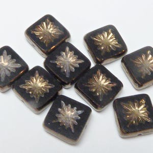 May include: A selection of dark brown square beads, each featuring a starburst design in gold and silver. The beads are displayed on a white surface, highlighting their detailed patterns and reflective qualities. These beads are suitable for crafting jewellery.